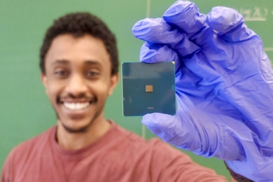 Natnael Kahssay, wearing nitrile gloves, smiles and holds up a computer chip for the camera.