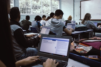 Group of high school students pictured sitting at desks with their back to the camera, typing on laptops
