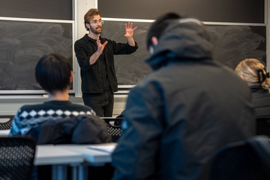 Michal Masny teaching in front of a blackboard in a classroom with students 