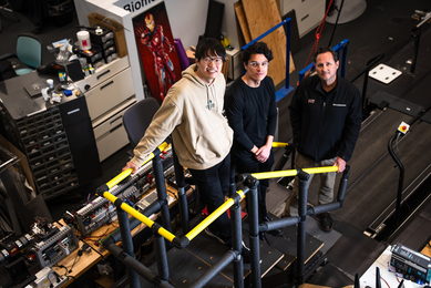Three men stand in a robotics lab