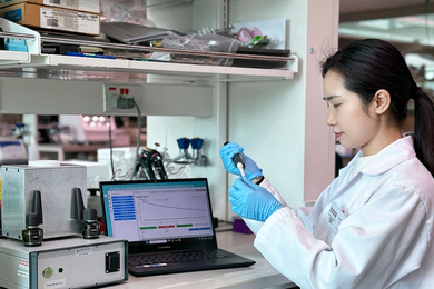 Yanmeng Yang, in lab coat and nitrile gloves, handles a sample in a wet lab