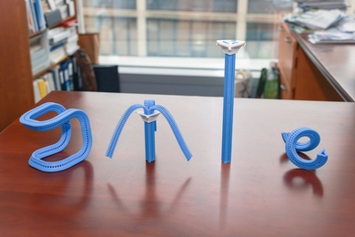 Four blue plastic zipper structures, each a unique shape, stand on a wooden office desk