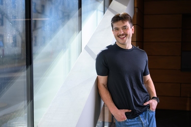 Perrin Davidson stands, posing, against an indoor staircase
