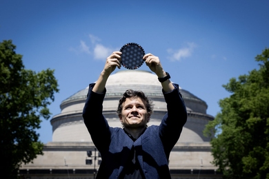 Pablo Jarillo-Herrero stands in front of the MIT dome, holding a circular wafer displaying moire patterns over his head