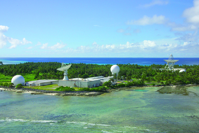 Two radar domes and two radar dishes sit on a tropical island on a sunny day