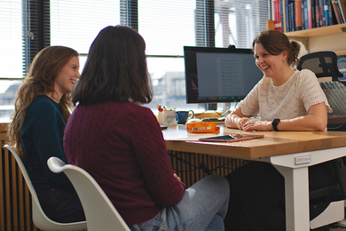 Anna-Christina Eilers sits at her desk, smiling at two women who sit facing her