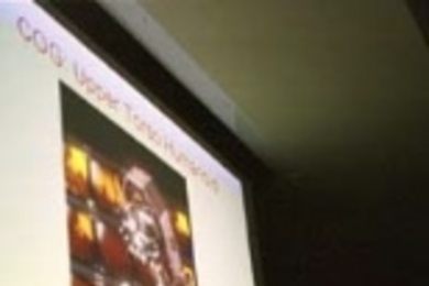 Rodney A. Brooks, director of the Artificial Intelligence Lab (AI Lab), gave the opening talk at the Humanoids 2000 Conference. On the screen is Cog, a humanoid robot developed at the AI Lab.