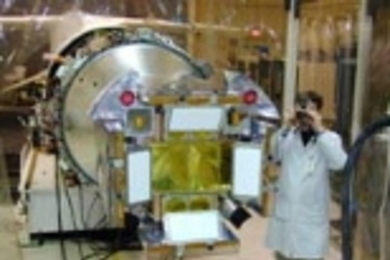 Dr. George R. Ricker, principal investigator for the High-Energy Transient Explorer satellite (HETE-2), takes a photograph during the final inspection of the satellite's soft X-ray cameras. The two dark circles are lens caps covering the optical cameras, and the two curved "ears" behind them are the soft X-ray cameras built at MIT. The four white rectangles on the satellite's front, which is small...