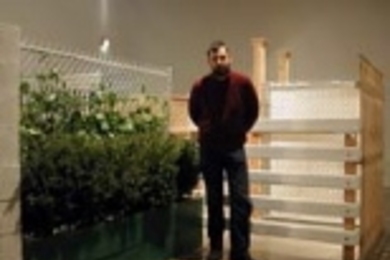List Center Curator Bill Arning stands beside Monica Bonvicini's Turning Walls, 2001, composed of plants and wooden metal and plastic fencing over a wooden armature.