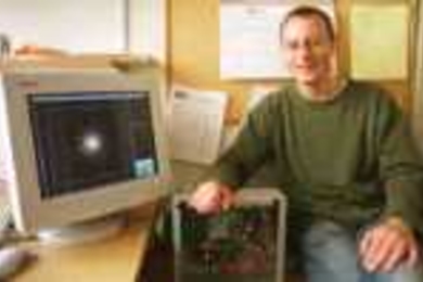 Simon Portegies Zwart rests his right hand on a prototype of the GRAPE-6, a computer he'll use to simulate star clusters (seen on monitor) and galactic nuclei.