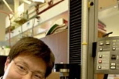 Chemical engineering research associate Yadong Wang stretches a piece of regular vulcanized rubber.  Biorubber, which is white and oaque, is stretched using the machine by his side.