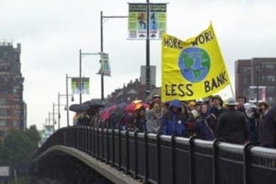 Activists cross the Massachusetts Avenue bridge from Boston to Cambridge to protest the policies of the World Bank during MIT's Commencement .