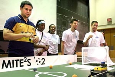 Teaching assistant Guillermo Chicas  (far left), watches the winning robot in action at the 2002 MITE 2S  Robotics Design Competition, held July 26. The team that designed and built the  machine included (left to right, wearing white) Cherelle Walls, Oyinade Aderibigbe,  Aaron Arizpe and Daniel Chaparro.