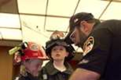 World Trade Center Task Force Fire Safety Director Mike Bellone helps Jamie Joyce, 8, into one of the jackets he and his fellow workers wore in their rescue efforts at the World Trade Center.  Jamie's brother Patrick, 10, stands nearby, outfitted in a similar jacket and hat.  The children's great-grandfather was a Somerville firefighter.  Their great-aunt Kathy Doyle works at Sloan School.