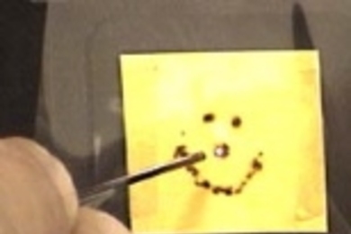 Members of the Fink lab use laser light- produced by a powerful carbon dioxide laser and transported through the new photonic bandgap fiber- to burn a smiley face in one of the materials that is used to make the fiber.