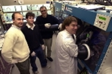 Vladimir Bulovic, assistant professor in electrical engineering and computer science, chemistry graduate student Jonathan Steckel and chemistry professor Moungi Bawendi (from left), watch as Seth Coe, a graduate student in electrical engineering and computer science, inspects a vial of fluorescing quantum dots in preparation for fabricating a light-emitting device.