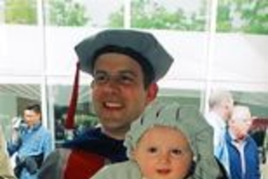 Six-month-old Miles Fox-Kempler, all dressed up in toddler-sized MIT regalia, relaxes in his father's arms at the hooding ceremony. Baylor Fox-Kemper received the Ph.D. in physical oceanography.