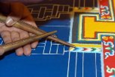 A Buddhist monk painstakingly creates a pattern in sand as he works on the Chenrezig Mandala, which symbolizes creation of the universe in a three-dimensional circular pattern. He gently scrapes an empty funnel held in his right hand along a sand-filled funnel in his left hand to carefully control how he places the sand. Monks created the mandala over several days in Simmons Hall.