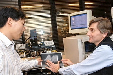 Postdoctoral associate Dae-Hyun Kim, left, and Professor Jesús del Alamo look at a cross-section of the new transistor they have been developing. Behind them is the test equipment used to measure its characteristics.