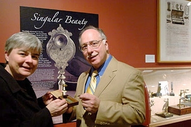 MIT Museum curator of science and technology Deborah Douglas examines a simple microscope from the exhibit, 'Singular Beauty,' with the owner of the collection, Raymond V. Giordano.