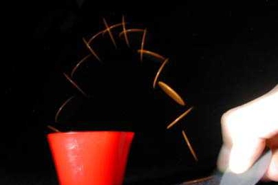 A tiddlywinks player uses a squidger to flip a wink into the cup.