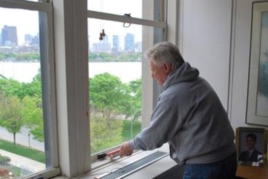 MIT Sloan School of Management Dean David Schmittlein uses caulk to seal up the windows in E52 to help conserve energy.