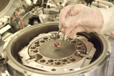 Graduate student Will Chung displays a hybrid chip being developed in Professor Tomas Palacios' lab. The machine in the background is used to combine the semiconductor materials into one chip.