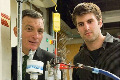 Professor Donald Sadoway and graduate student David Bradwell observe one of their small test batteries in the lab. The battery itself is inside the heavily insulated metal cylinder at center, which heats it to 700 degrees Celsius, while the wires at top charge up the battery and measure its performance.