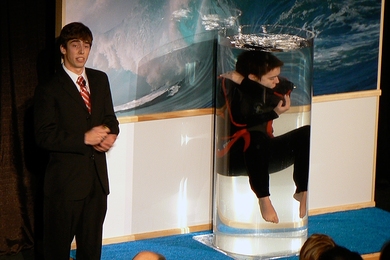 Taylor Williamson floats in a tank of water to demonstrate emergency breathing device, while her teammate Chris Peters explains the invention, at the final presentations for class 2.009.