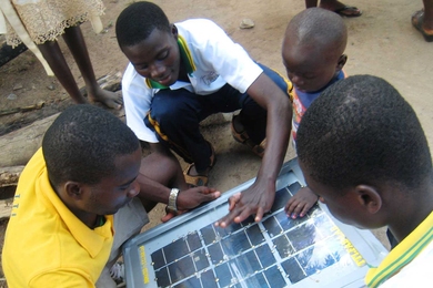 Three students from the Ghana Fab Lab put the finishing touches on a solar panel unit in Kobina Adorh Krom village, with help from a young friend.