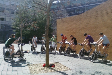 Lauren Hanley, assistant director of fitness for DAPER, left, takes advantage of the warmer weather and takes her group cycling class outside of the Wang Fitness Center.