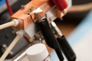 A sample of 'Cambridge crude' — a black, gooey substance that can power a highly efficient new type of battery. A prototype of the semi-solid flow battery is seen behind the flask. 