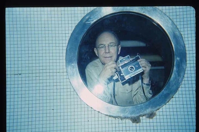 Harold “Doc” Edgerton holds a Polariod camera while photographed from inside the MIT pool.