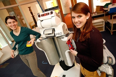 Jennifer Barry (left) and Annie Holladay pose with the Learning in Intelligent System Group's PR2 robot.