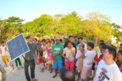 People gathered outside, one of whom is holding up a solar panel