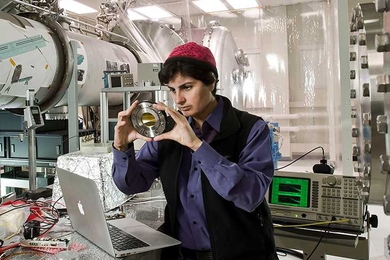 Nergis Mavalvala stands in a lab looking at a small electronic device