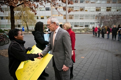 Student holds poster and shakes L. Rafael Reif's hand 