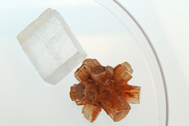 Two different forms of calcium carbonate have identical chemical composition, but look different and have different properties such as solubility. The flat, clear crystal is calcite, the pinkish multifaceted one is aragonite.