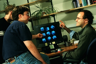 Three people speaking around computer at desk