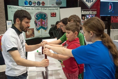 Ted Golfinopoulos (left), a postdoc with MIT’s Plasma Science and Fusion Center, invites visitors to the USA Science and Engineering Festival to feel how insulated copper coil gets warm when electrical current runs through it, in a demonstration about magnetism and electricity.