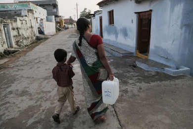 A woman and her son, who live in Chellur, India, walk home with the reverse-osmosis-treated water she bought at Chellur’s community desalination plant.
