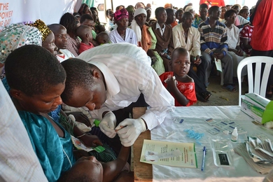 Women and children in rural Uganda look on as a service provider from a nearby health center provides malaria tests for communities on the lake's edge.