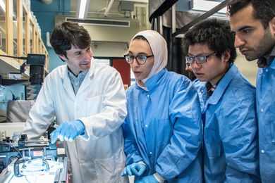Associate Professor Ruben Juanes (left) and students (l-r) Lubna Barghouty, Yunteng Cao, and Ehsan Haghighat discuss the impact of wettability on the patterns of fluid invasion into a porous microfluidic chip, illuminated from below and recorded with a high-speed camera from above. 
