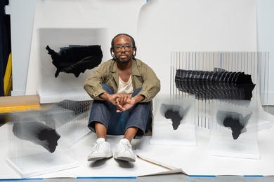 Artist Ekene Ijeoma sits with “​Pan-African AIDS,” a sculpture representing the hyper-visibility of the HIV/AIDS epidemic in Africa and the hidden one in Black America.
