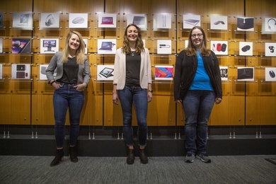 Left to right: Ann McInroy ’18, Isabella Didio ’16, and Jacklyn Herbst ’10, MEngM ’11 stand in front of a wall showing the history of Microsoft’s hardware since the 1980s in Building 88 of Microsoft’s campus located in Redmond, Washington.