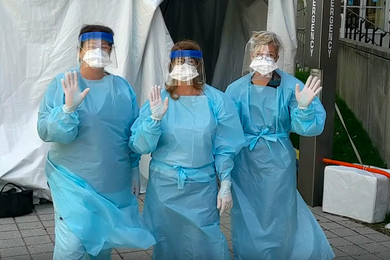 Three MIT Medical workers in full protective coverings wave to the camera