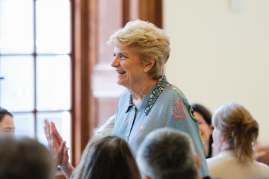 Nancy Hopkins smiling while about half a dozen others, seated around her, applaud