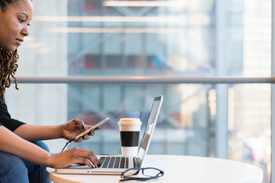 Photo of a woman, seated with a smartphone and laptop