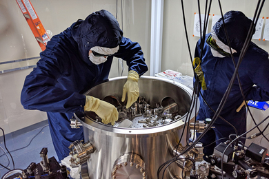 Photo of two people in clean suits inspecting a mirror-testing apparatus