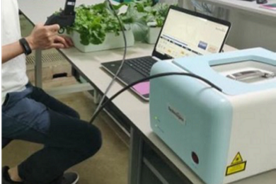 Photo of a desk in a laboratory, with an open laptop and a boxy machine that looks like a printer